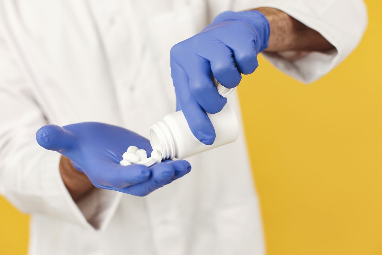 Close-up of a healthcare worker in gloves pouring pills from a bottle.